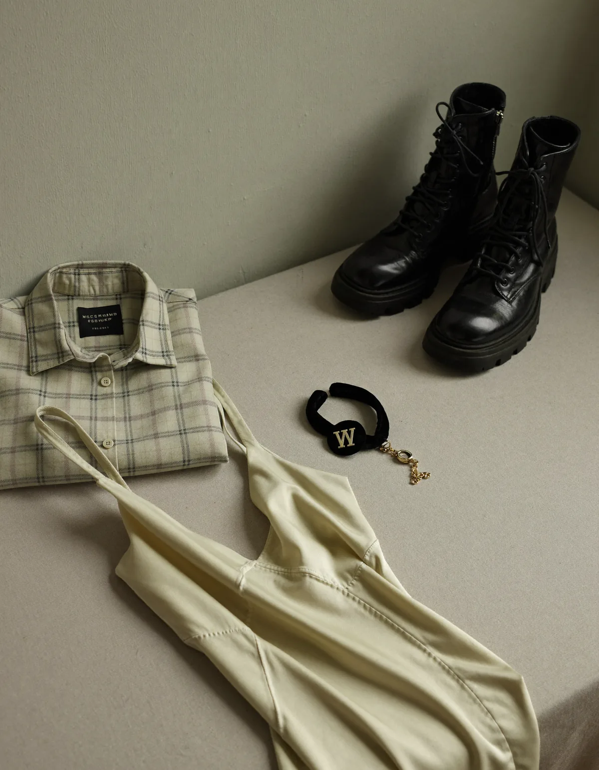 A folded plaid flannel shirt, a satin slip dress, chunky black boots and a velvet choker on pale oyster linen