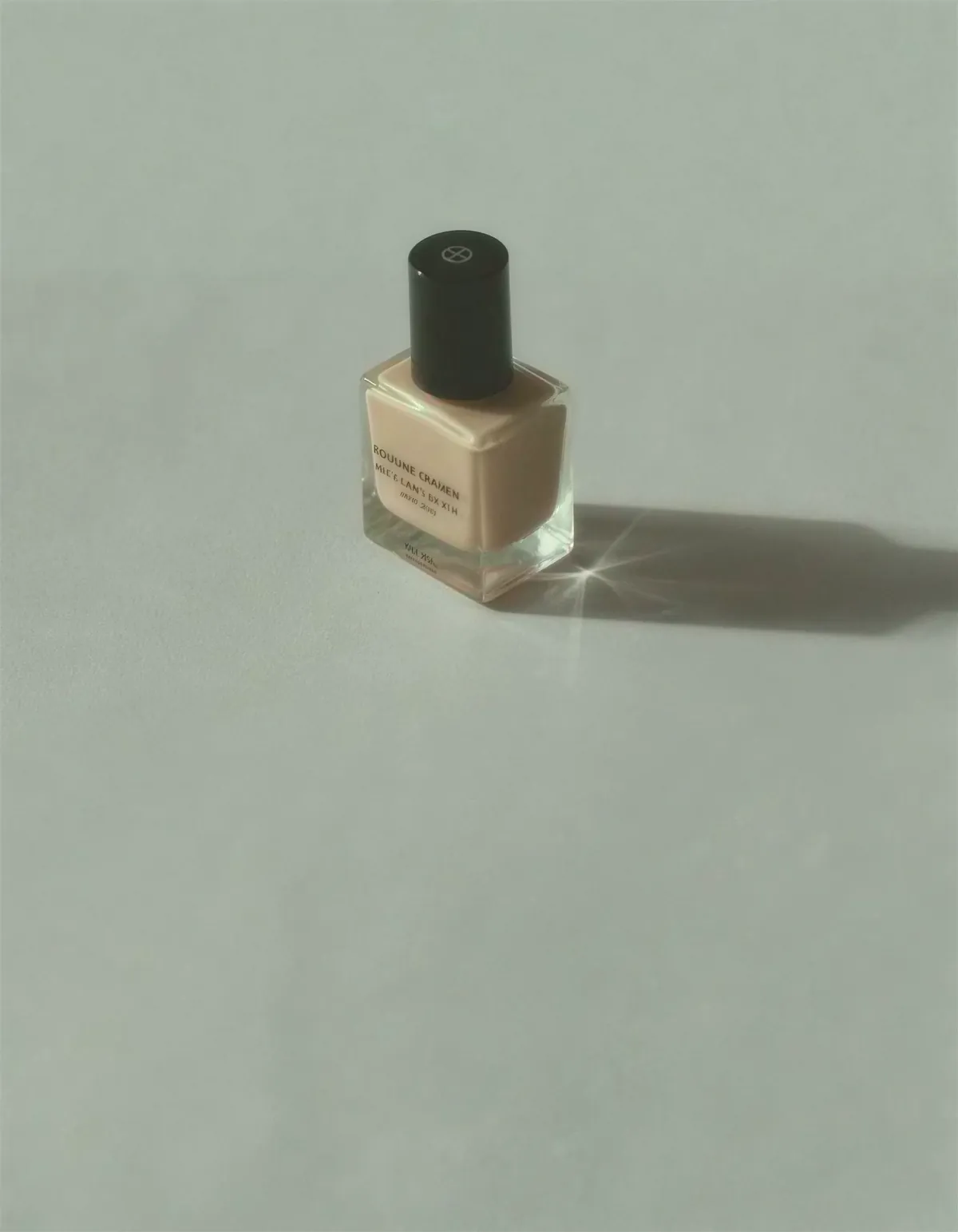 A frosted glass nail polish bottle on pale gray seamless with a long soft shadow