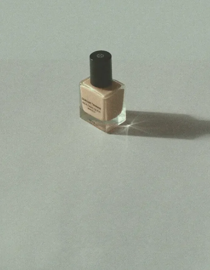 A frosted glass nail polish bottle on pale gray seamless with a long soft shadow