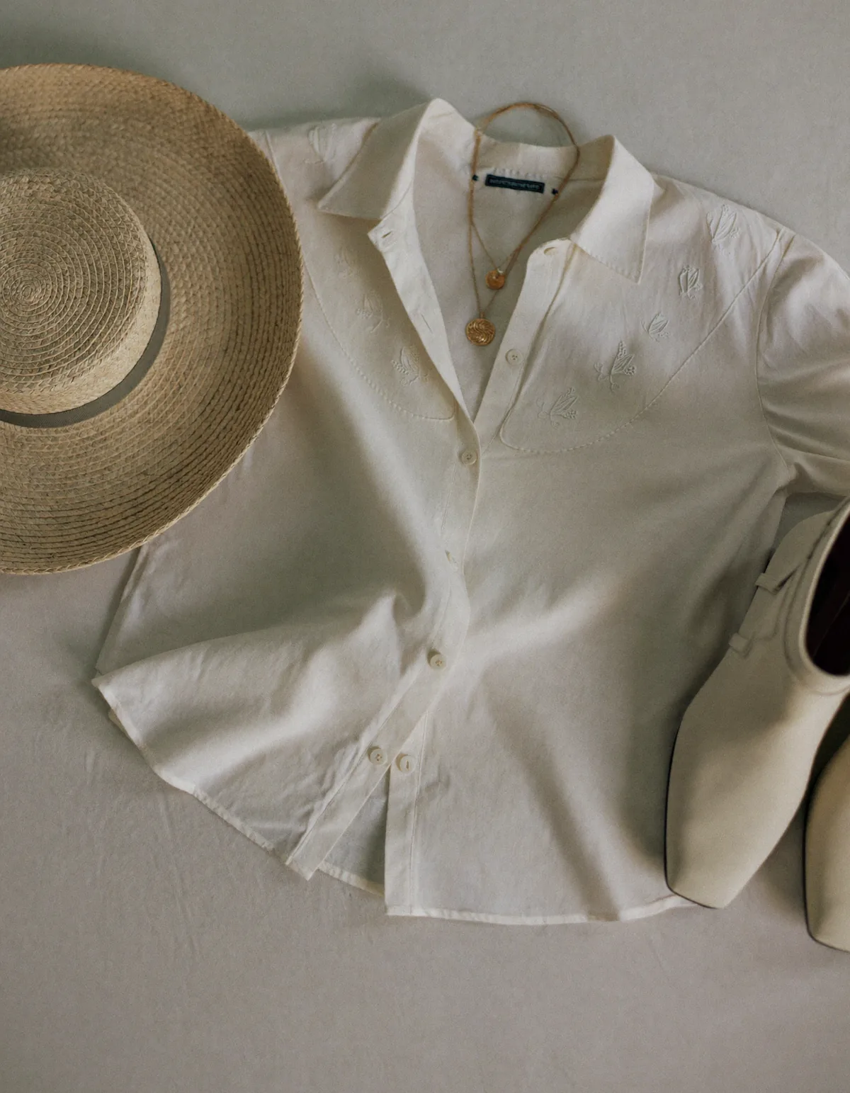 A cream embroidered cotton blouse, suede ankle boots, a wide-brim straw hat and layered gold necklaces