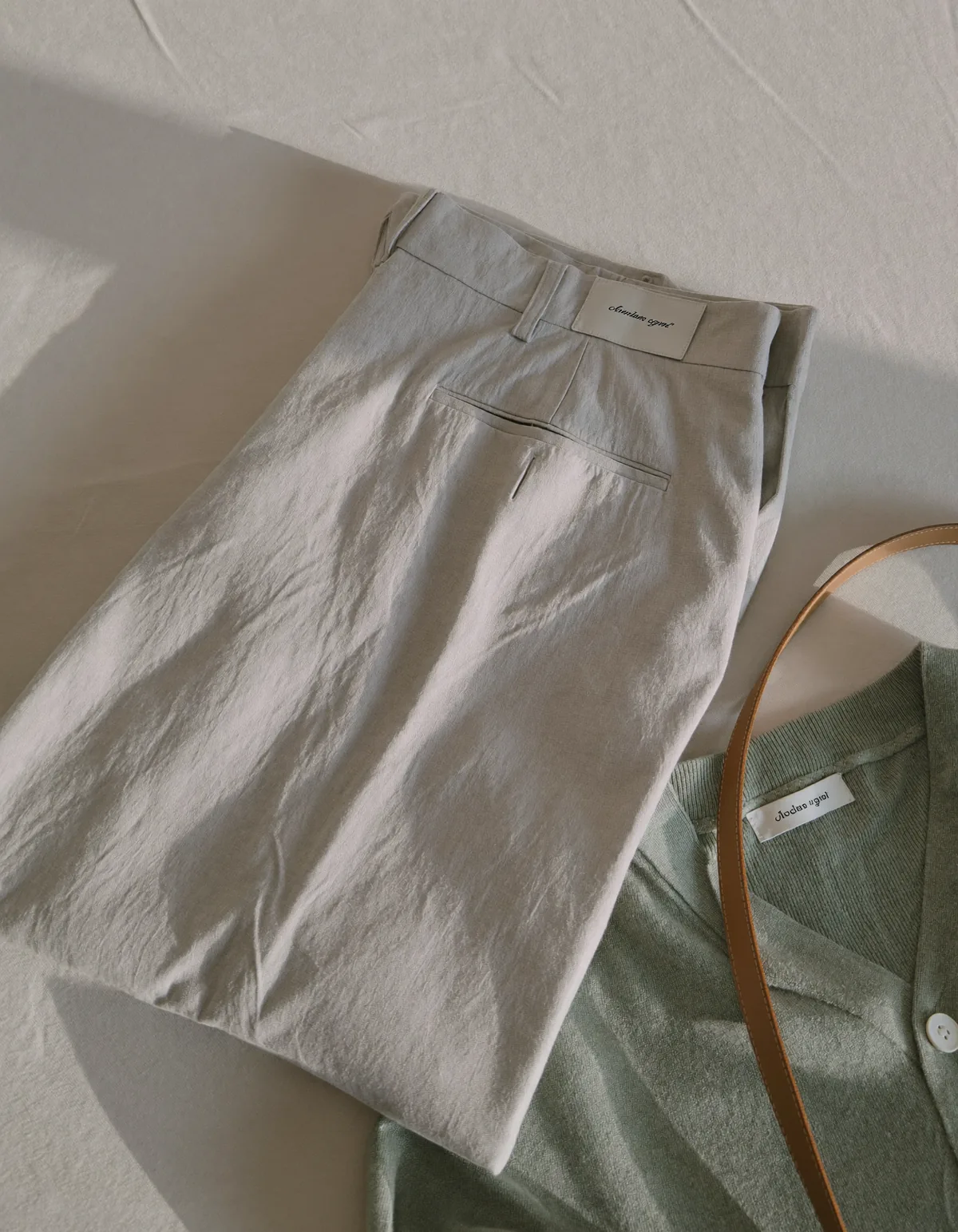 Pressed ivory wide-leg trousers, a fine-knit sage cardigan and a slim tan leather belt on pale oyster linen
