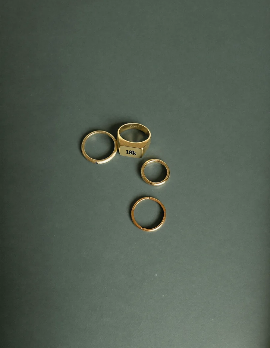 Three fine gold rings in 14k and 18k tones arranged on a pale oyster surface