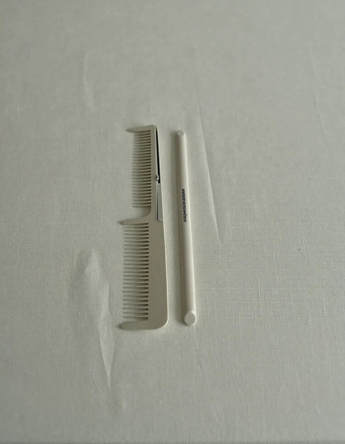 Two slim cream-colored hair styling tools lying parallel on pale oyster linen