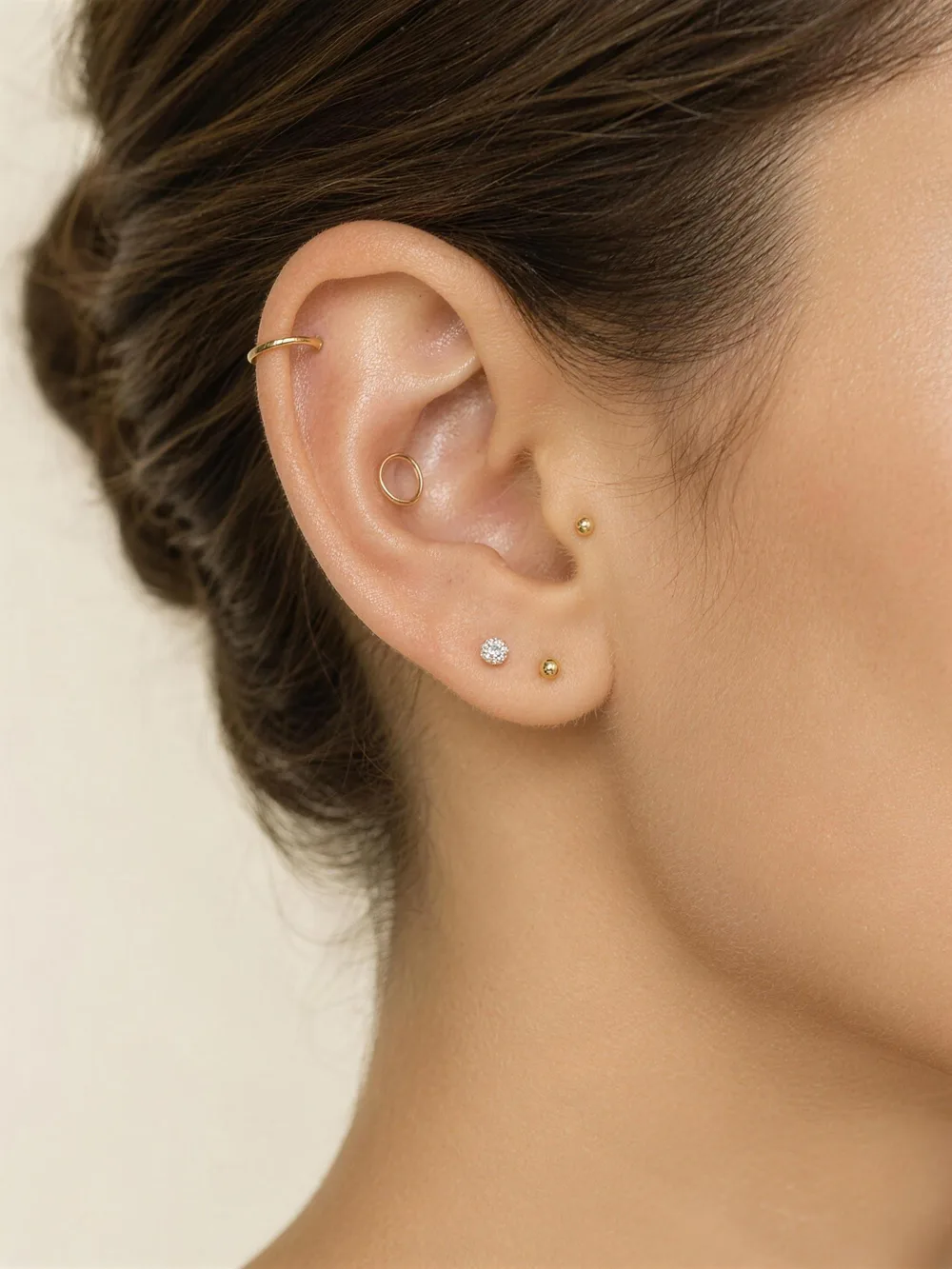 Close-up of a curated gold ear with a diamond stud and a gold stud in the lobe, a slim helix hoop, a conch ring and a small stud