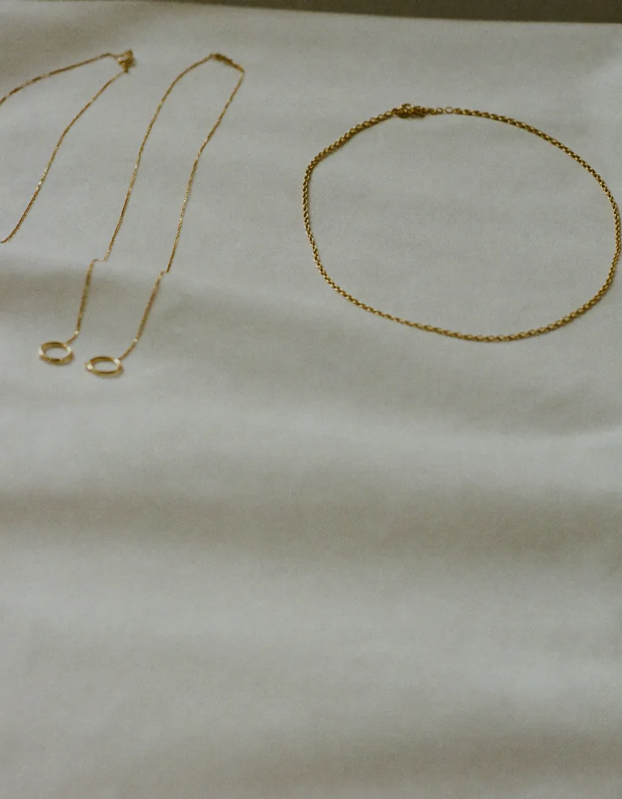 Three fine gold chains and a pair of small gold hoops arranged on pale oyster linen