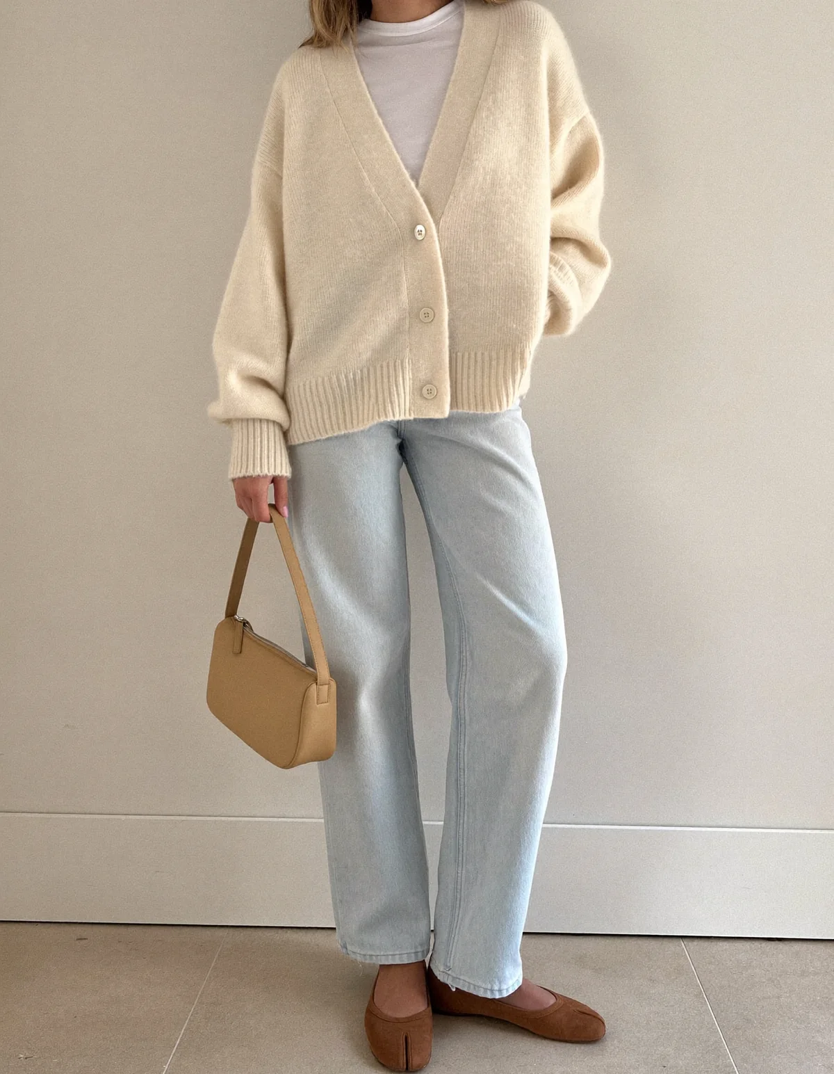 A woman on an autumn sidewalk in a beige trench coat, cream knit, dark straight jeans and brown loafers