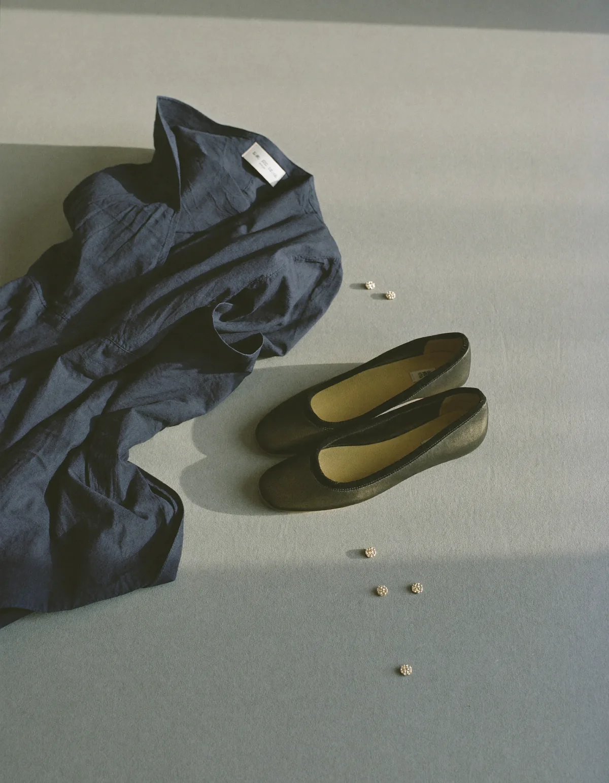 A folded dark navy crepe dress, plain black flat shoes and small pearl stud earrings on pale oyster linen