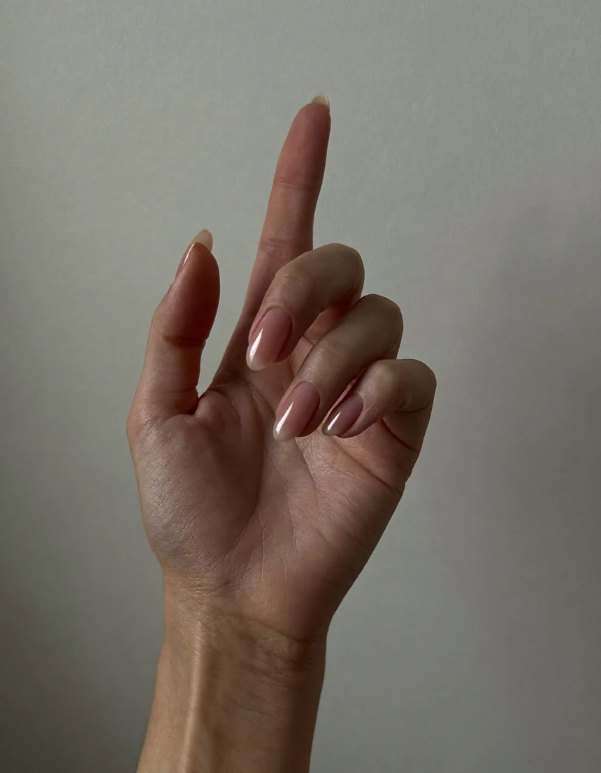 A raised hand with soft rose semi-cured gel almond nails against a pale oyster backdrop