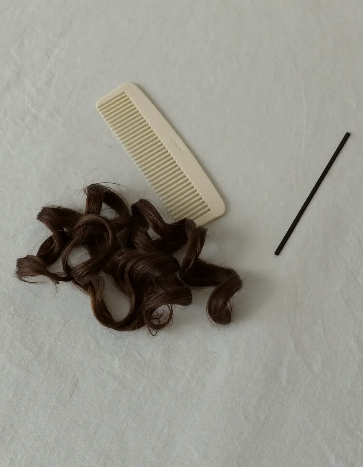 A soft coil of glossy dark brown wavy hair beside a wide-tooth comb and a flat elastic band
