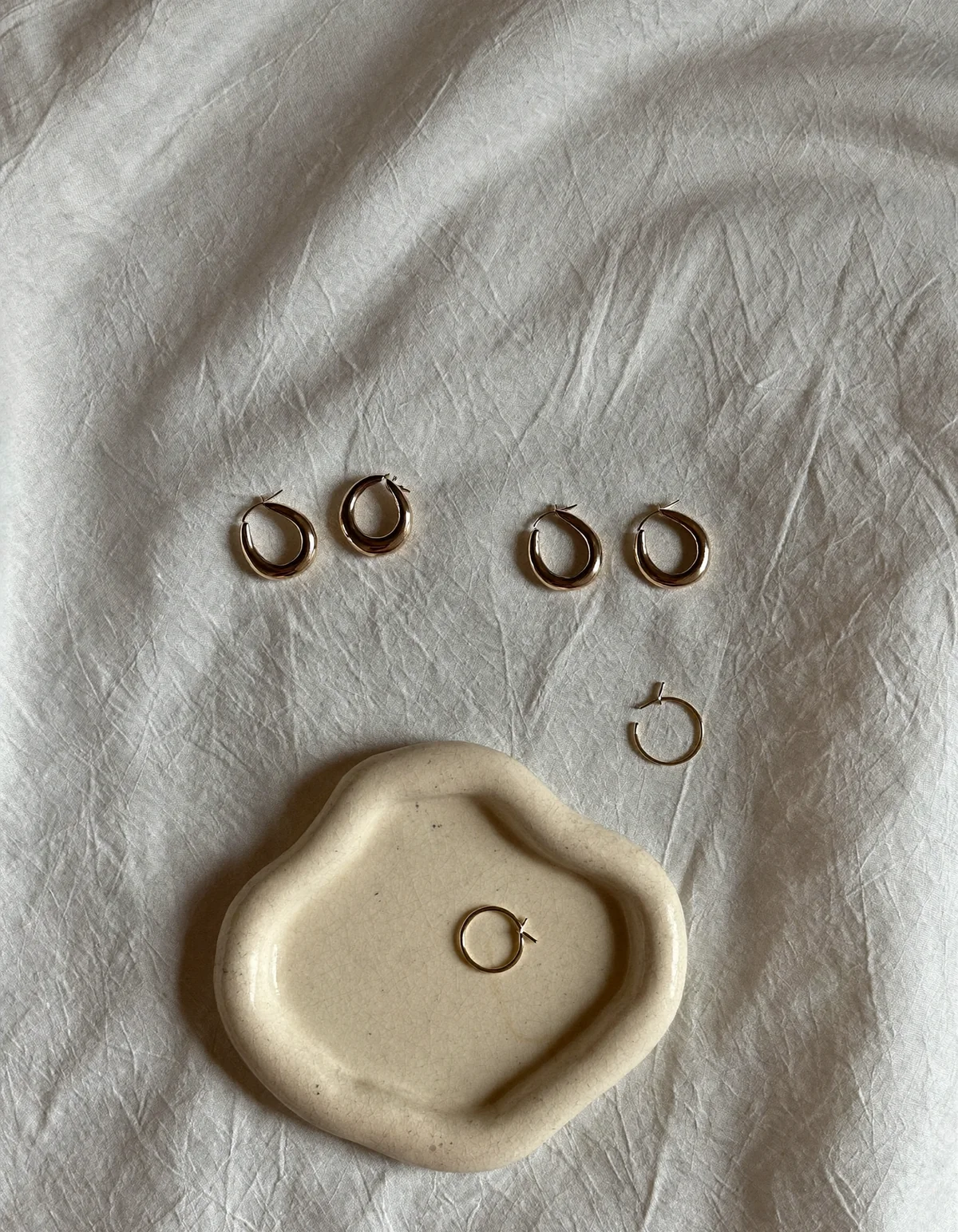 Gold hoop earrings in sizes from tiny huggies to large thin hoops laid on pale oyster linen
