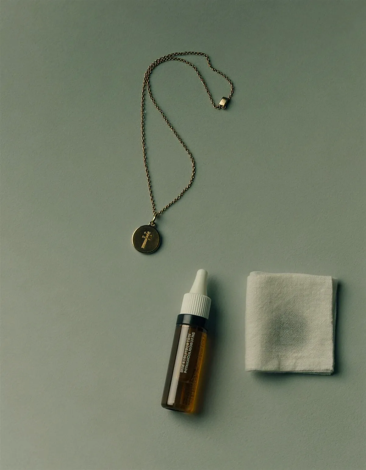 A fine gold pendant necklace beside a small amber dropper bottle and a folded test cloth