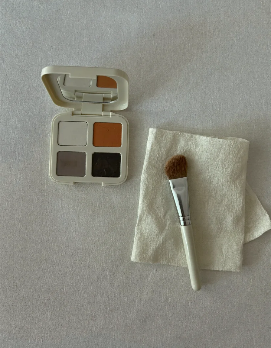 An open cream face paint palette in ivory, charcoal and soft pumpkin beside a fine brush