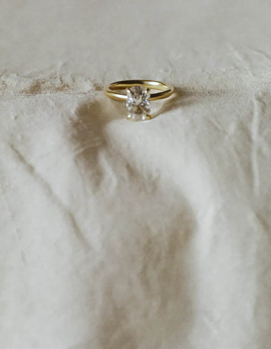 A solitaire diamond ring with a slim gold band resting on pale oyster linen in soft daylight