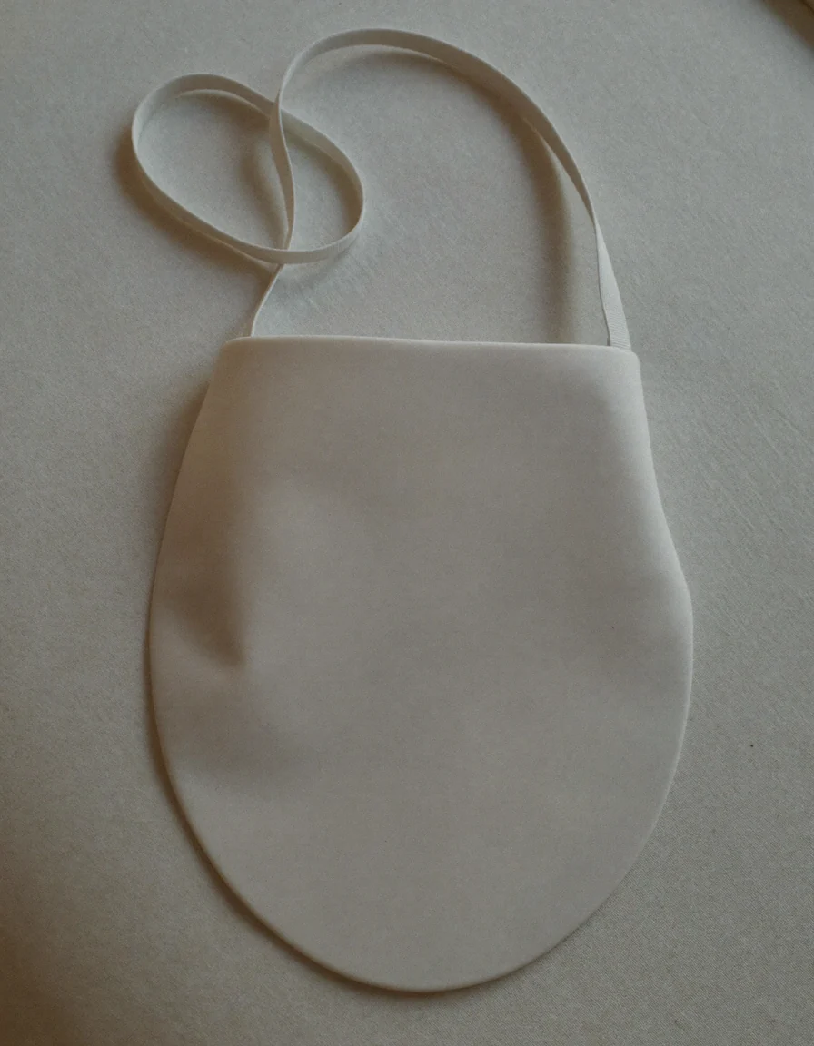 A smooth matte white light therapy face mask lying face up with its strap coiled beside it