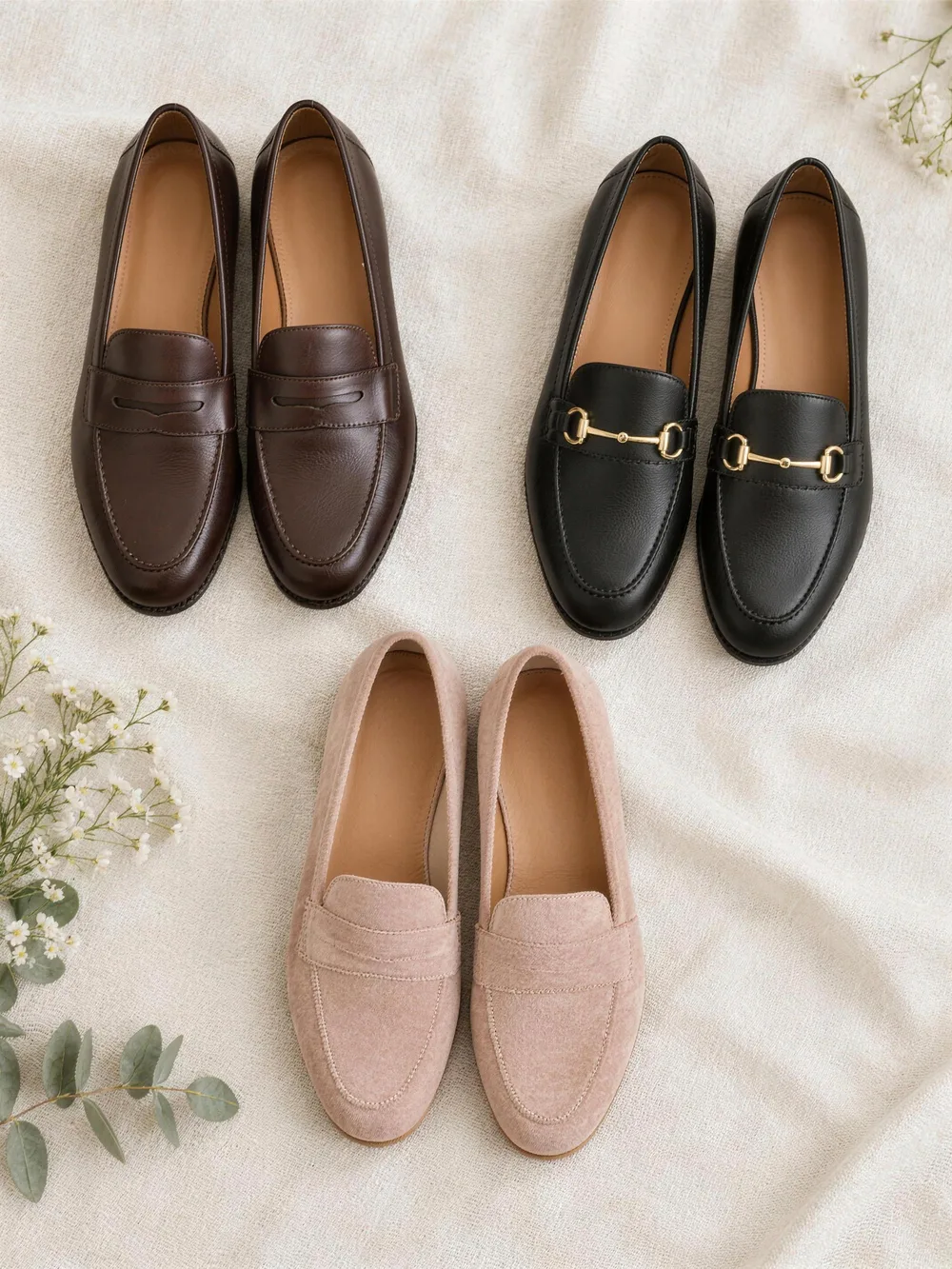 Three pairs of women's loafers on cream linen: dark brown penny loafers, black horsebit loafers and blush suede loafers