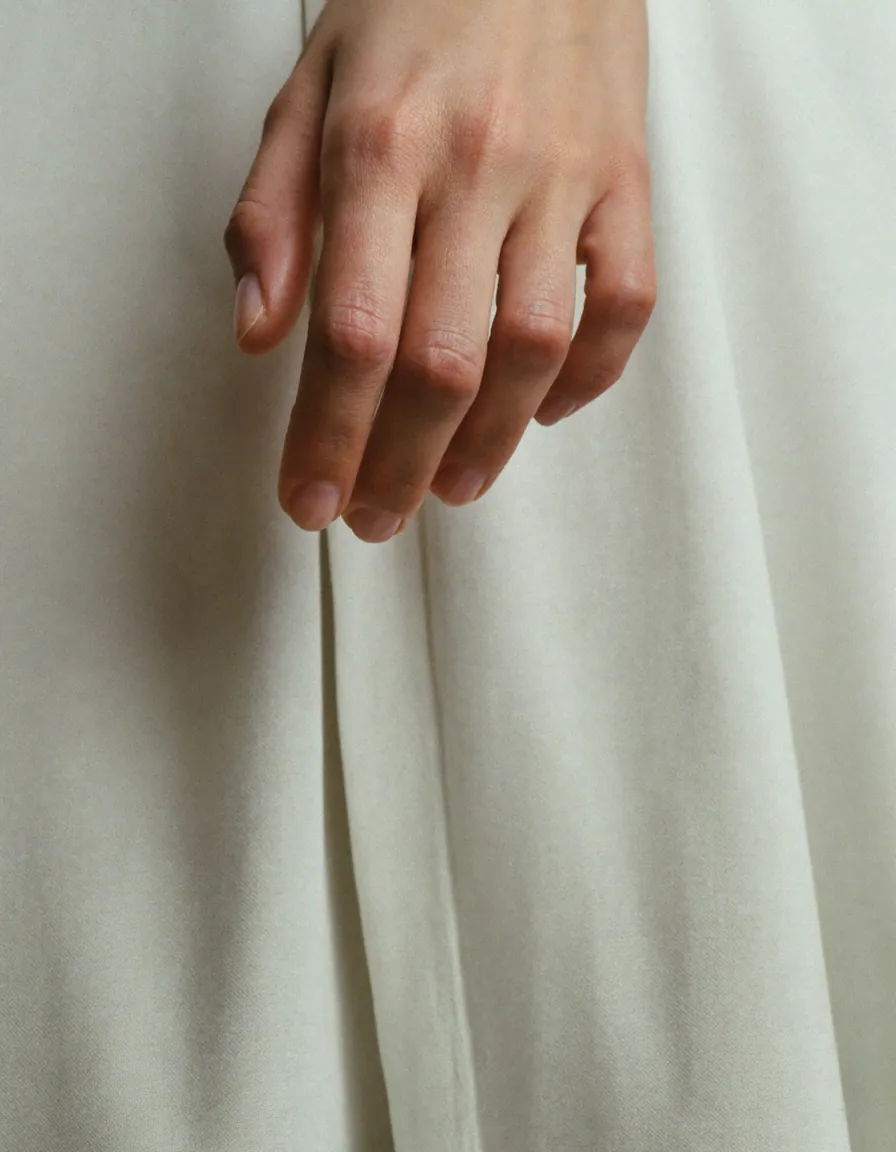 A relaxed hand resting against soft ivory cloth, nails bare and unpolished in their natural almond shape