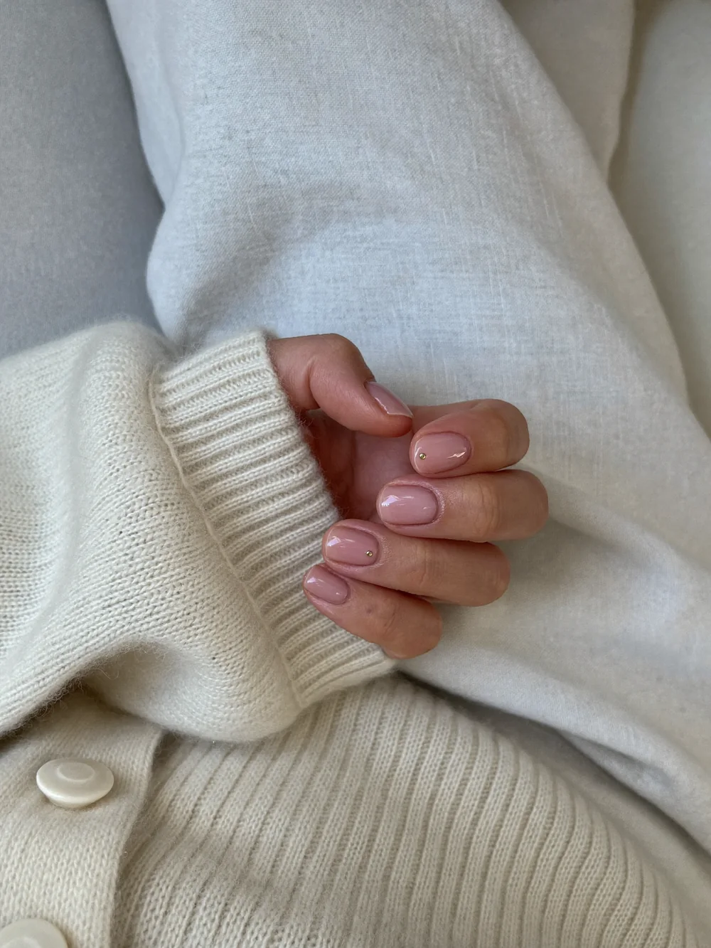 A relaxed hand with short sheer nude nails, each with one tiny gold dot near the cuticle