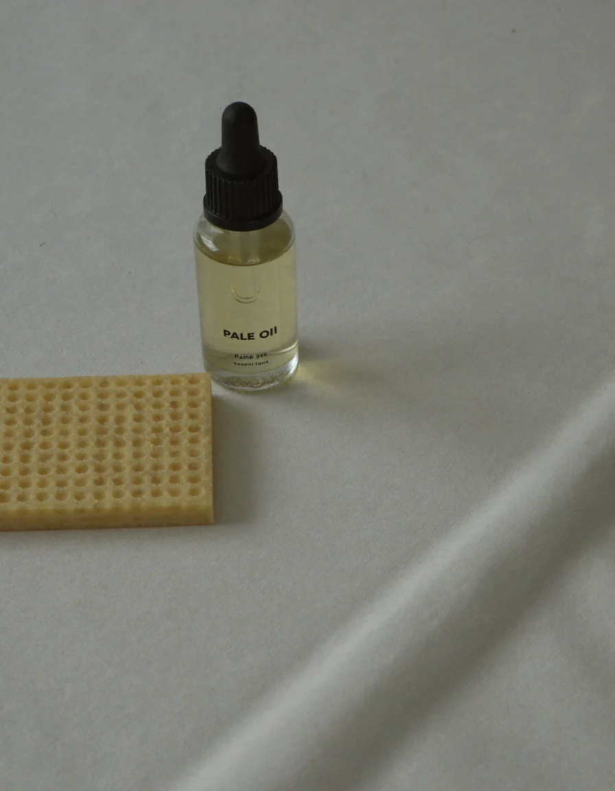 A small clear glass dropper bottle of pale oil lying beside a fine emery board