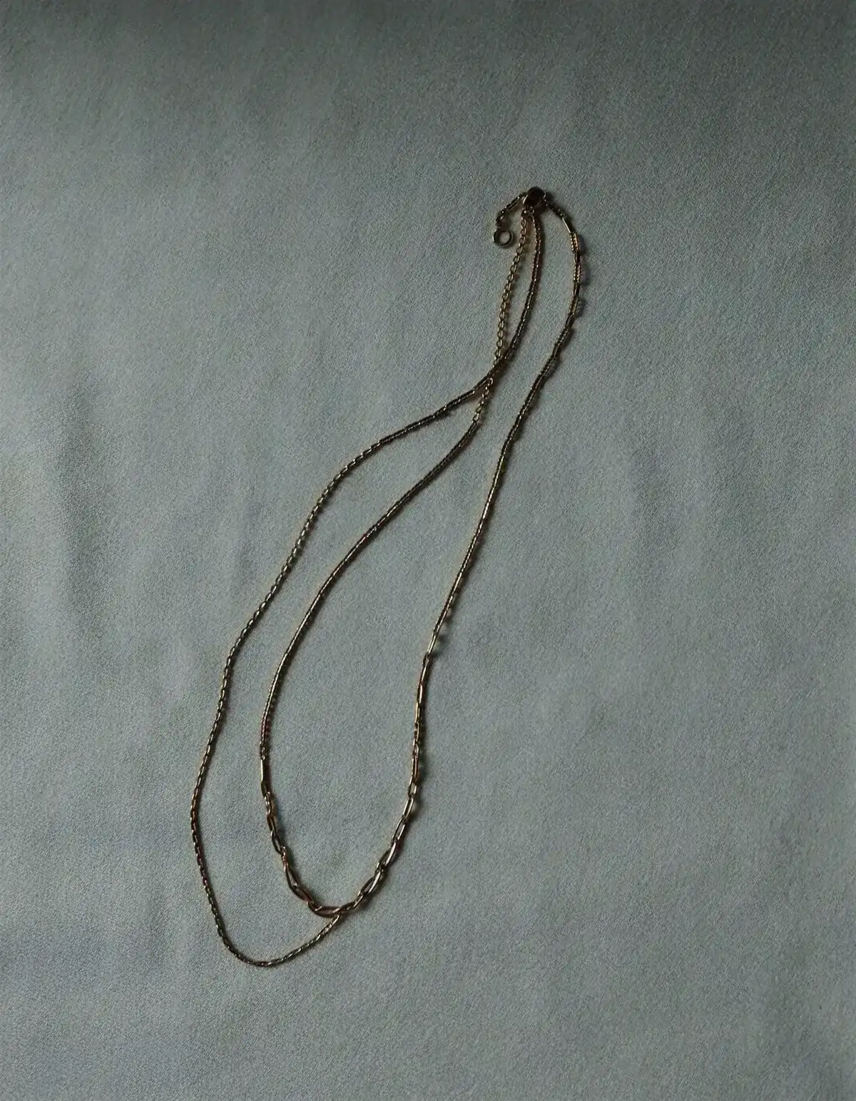 Two fine gold chain necklaces of different lengths layered on pale oyster linen