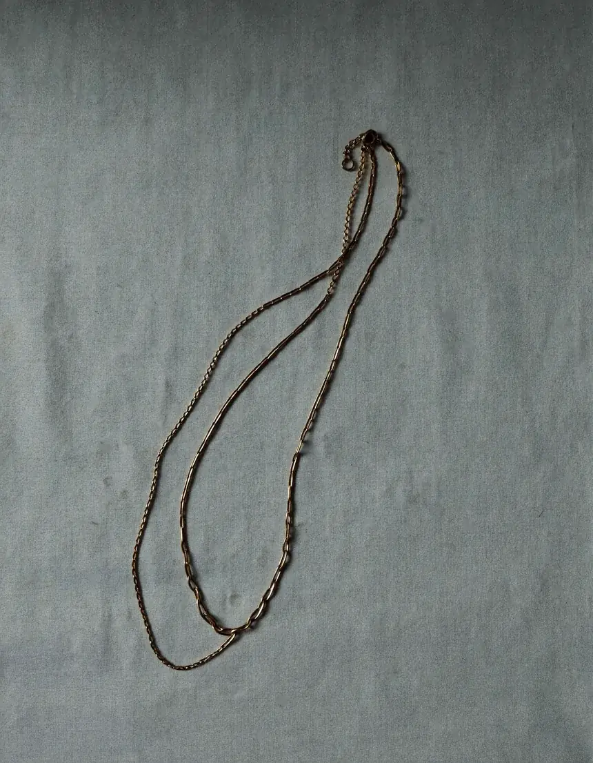 Two fine gold chain necklaces of different lengths layered on pale oyster linen
