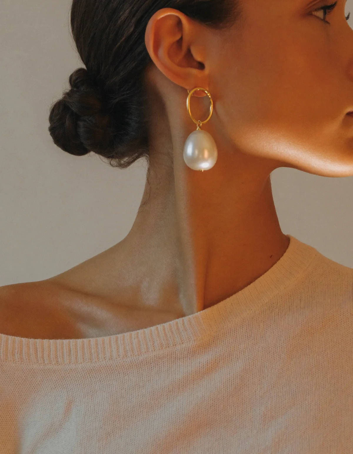 A woman in profile with a sleek low bun wearing a lustrous white pearl drop earring on a fine gold hook