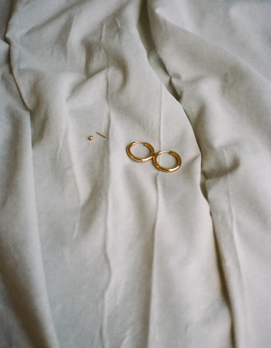 A pair of small gold hoops and two tiny gold studs resting on pale oyster linen