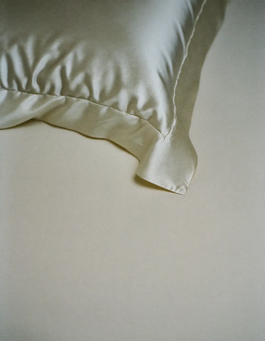 A softly folded corner of ivory silk catching low daylight on a pale oyster surface