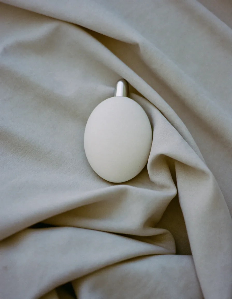 A small matte white skincare device resting on softly rumpled pale oyster linen