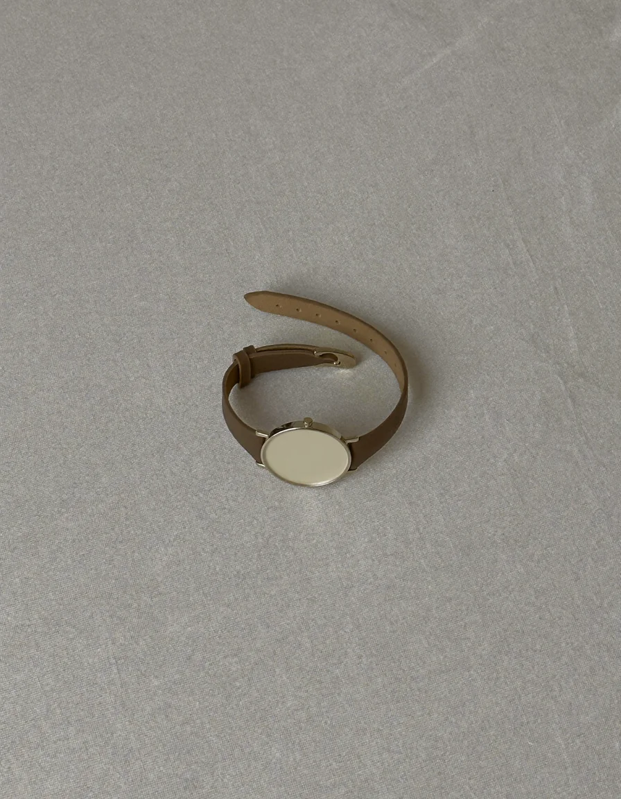 A slim wristwatch with a small round ivory dial on a fine taupe leather strap