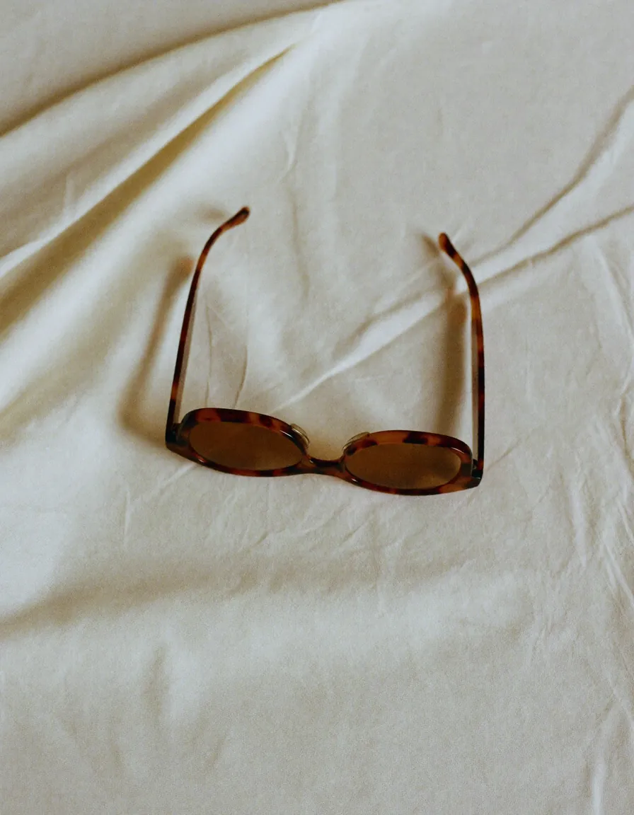 A pair of fine tortoiseshell sunglasses folded closed on pale oyster linen