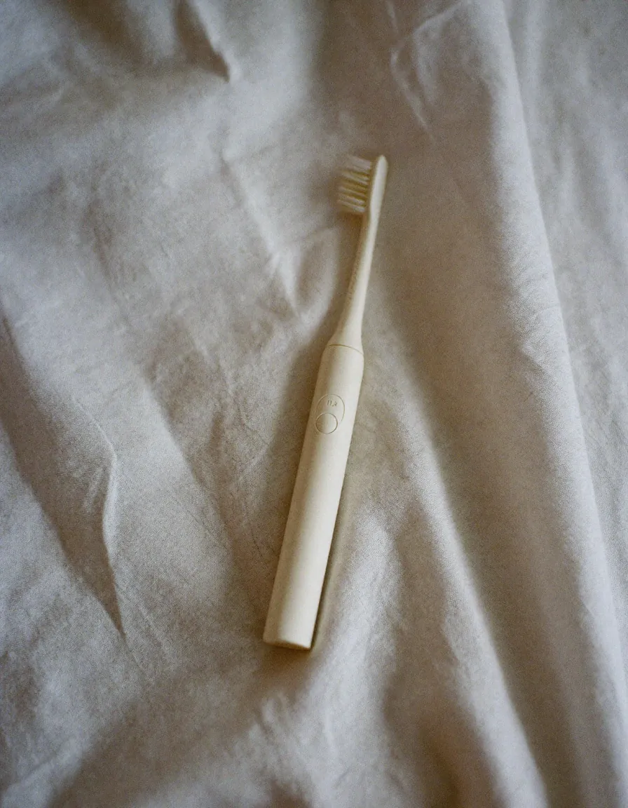 A slim plain white electric toothbrush lying at an angle on pale oyster linen