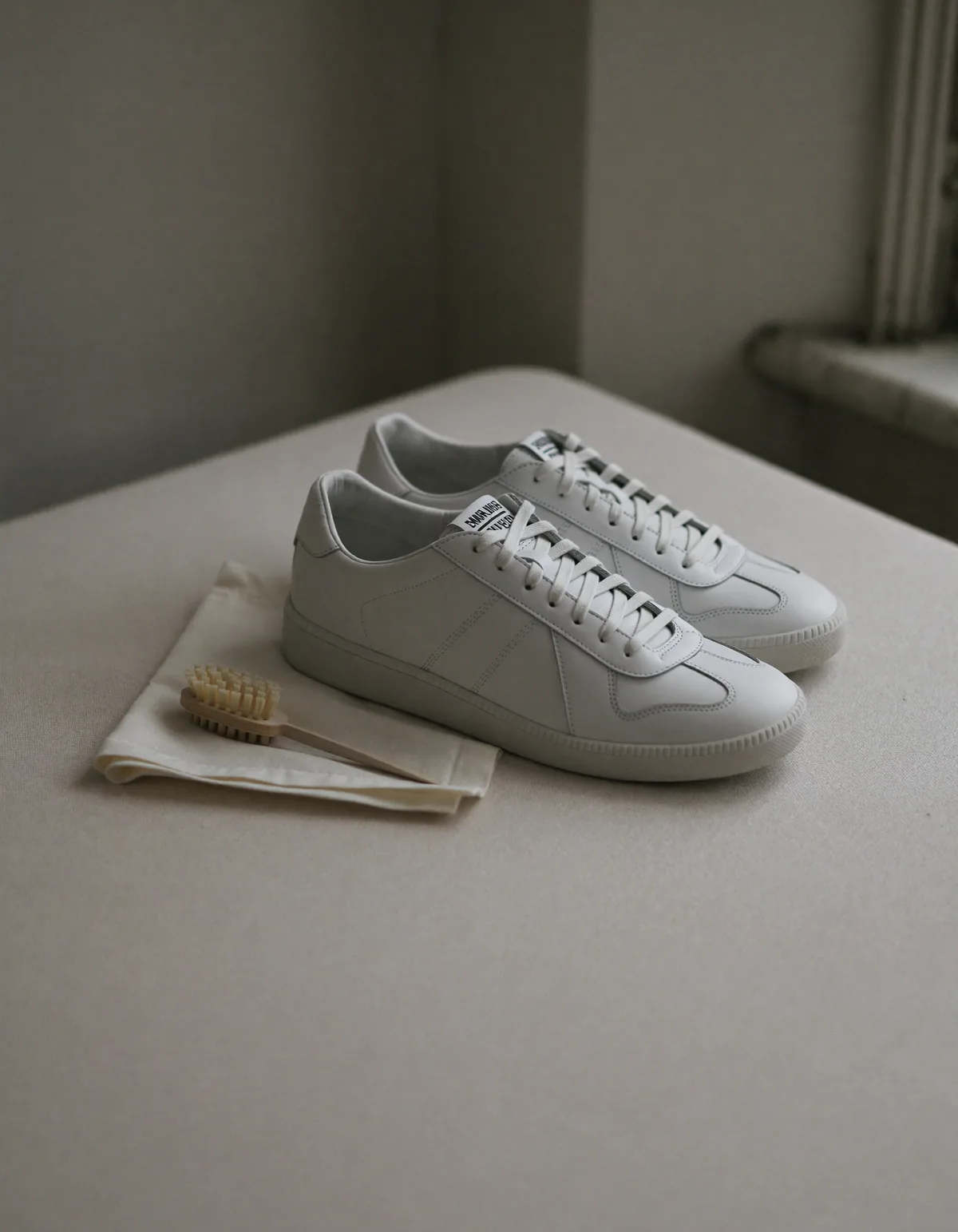 A pair of clean white leather low-top sneakers on pale oyster linen