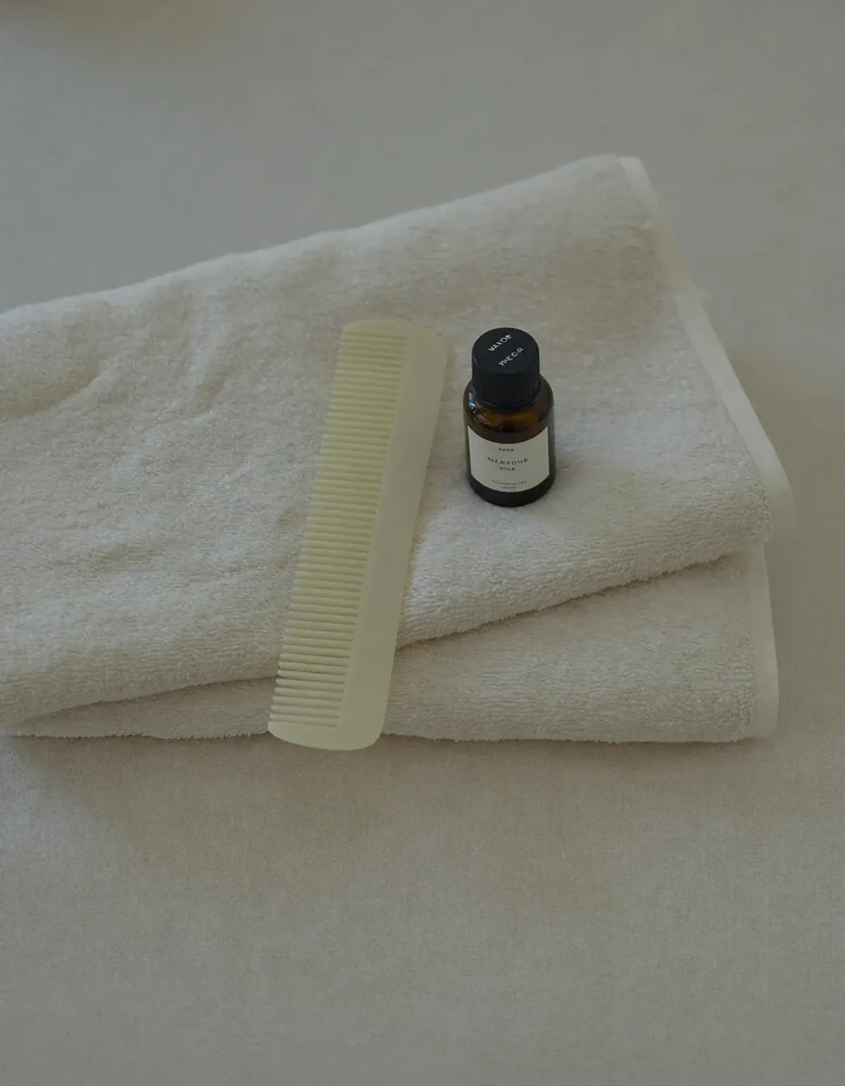 A plain wide-tooth comb and a small amber glass bottle resting on a folded ivory towel