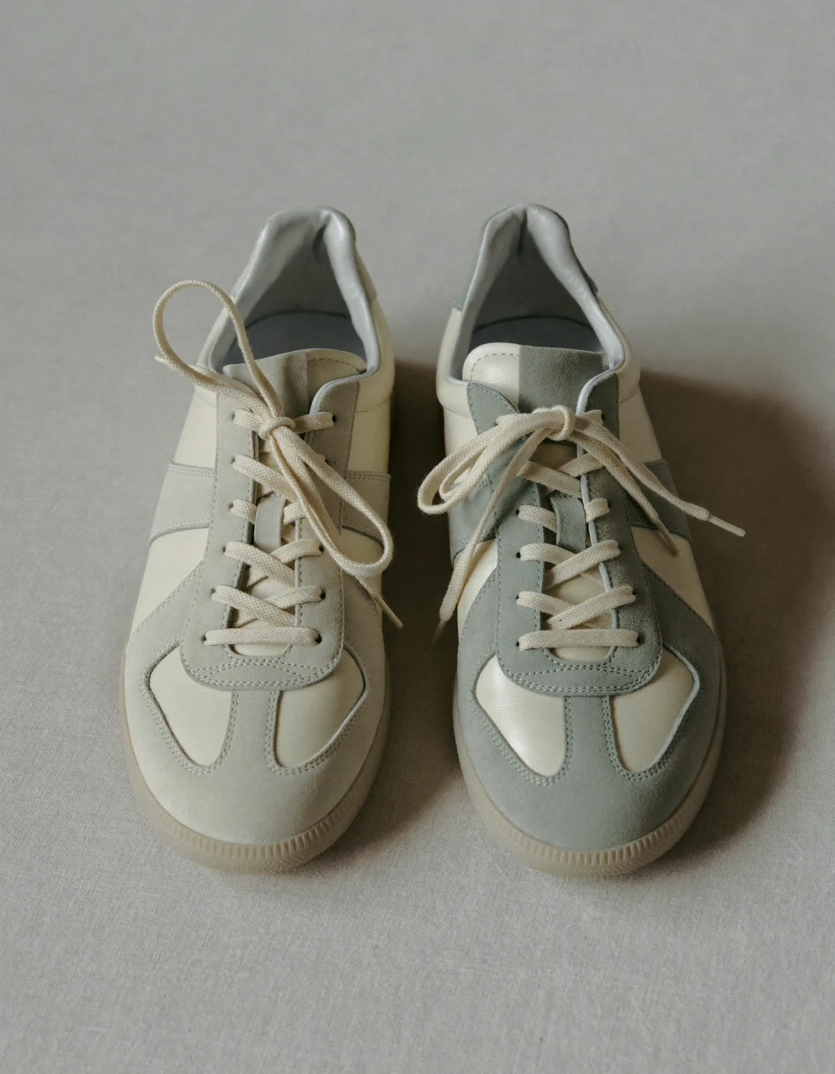 A pair of clean low-top sneakers on pale oyster linen in soft daylight